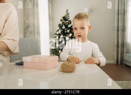 Un garçon prépare des cadeaux pour Noël. Cadeau sur la table. La bougie brûle. Banque D'Images