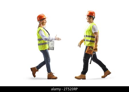 Plan de profil en longueur d'une femme ingénieur marchant et saluant un travailleur de la construction isolé sur fond blanc Banque D'Images