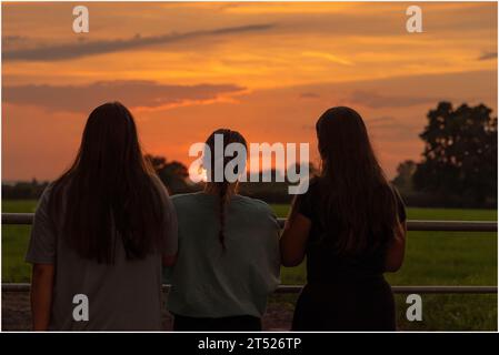 Trois filles debout regardant le coucher du soleil par agate avec héritier dos à la caméra Banque D'Images