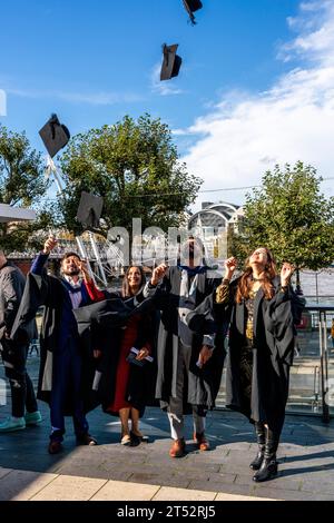 Les étudiants de diplôme jettent leurs chapeaux de panneau de mortier dans l'air à leur cérémonie de remise des diplômes, The Southbank, Londres, Royaume-Uni. Banque D'Images