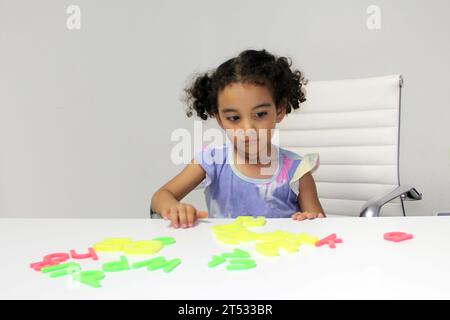 Une fille Latina de 3 ans aux cheveux bruns et bouclés joue avec un jeu de lettres et de chiffres pour un meilleur apprentissage dans le spectre de l'autisme Banque D'Images