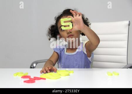 Une fille Latina de 3 ans aux cheveux bruns et bouclés joue avec un jeu de lettres et de chiffres pour un meilleur apprentissage dans le spectre de l'autisme Banque D'Images