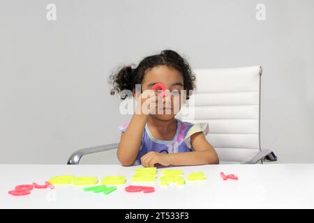 Une fille Latina de 3 ans aux cheveux bruns et bouclés joue avec un jeu de lettres et de chiffres pour un meilleur apprentissage dans le spectre de l'autisme Banque D'Images