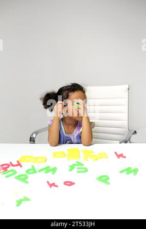 Une fille Latina de 3 ans aux cheveux bruns et bouclés joue avec un jeu de lettres et de chiffres pour un meilleur apprentissage dans le spectre de l'autisme Banque D'Images