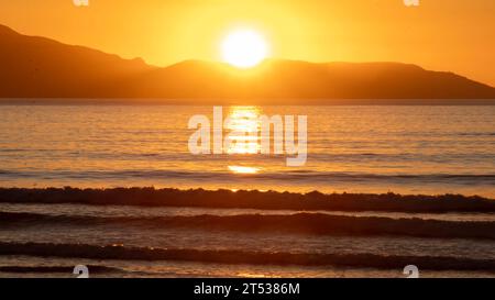 Golden Hour Serenity : le soleil d'or plonge sous l'horizon avec l'eau au premier plan au coucher du soleil sur la côte néo-zélandaise de Spirits Bay Banque D'Images