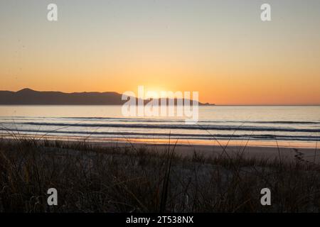 Golden Hour Serenity : le soleil d'or plonge sous l'horizon avec l'eau au premier plan au coucher du soleil sur la côte néo-zélandaise de Spirits Bay Banque D'Images