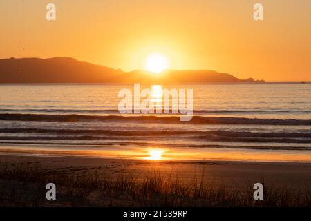 Golden Hour Serenity : le soleil d'or plonge sous l'horizon avec l'eau au premier plan au coucher du soleil sur la côte néo-zélandaise de Spirits Bay Banque D'Images