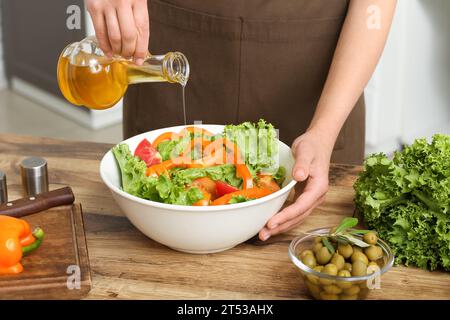 Femme ajoutant l'huile d'olive dans le bol avec salade savoureuse à la table dans la cuisine Banque D'Images