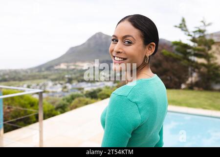 Portrait de femme biracial heureuse avec piscine dans le jardin à la maison Banque D'Images