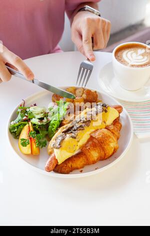 Sandwich brioche aux œufs croissants et saucisses avec fruits et légumes frais dans un café. Banque D'Images