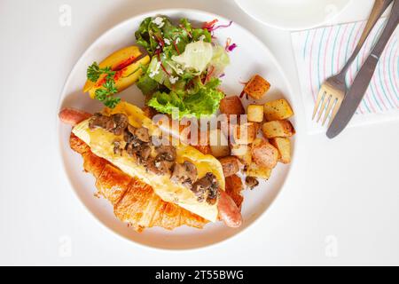 Sandwich brioche aux œufs croissants et saucisses avec fruits et légumes frais dans un café. Banque D'Images