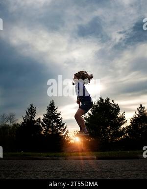 Jeune fille rebondissant sur le jouet de printemps au coucher du soleil Banque D'Images