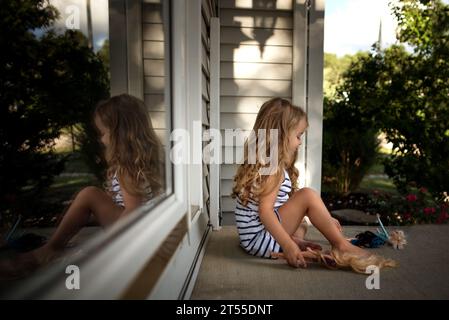 Petite fille avec de longues boucles jouant avec des poupées sur le porche Banque D'Images