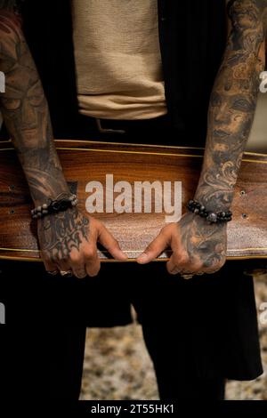 Homme tenant une planche à roulettes, main tatouée. Banque D'Images