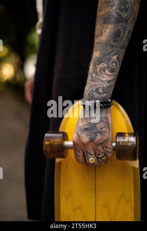 Homme tenant une planche à roulettes, main tatouée. Banque D'Images