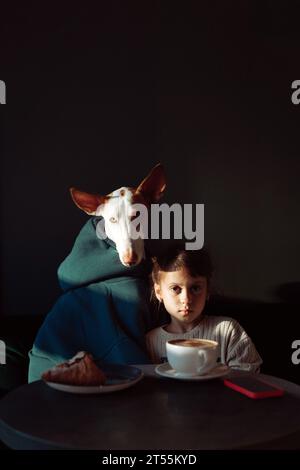 Fille enfant avec un ami chien dans le café, café, croissants, amitié. Banque D'Images