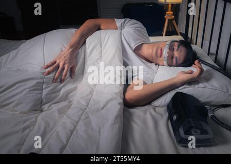 Homme asiatique heureux et en bonne santé avec la machine CPAP sur la table d'appoint portant le masque CPAP dormant en douceur dans le lit toute la nuit sans ronfler Banque D'Images