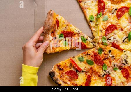 La main féminine prend un morceau de pizza. Vue à angle élevé de pizza au pepperoni et basilic. Banque D'Images