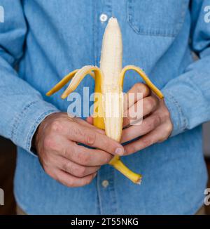 Gros plan banane jaune dans les mains masculines. L'homme tient une banane dans ses mains devant lui. Peler la banane. Banque D'Images