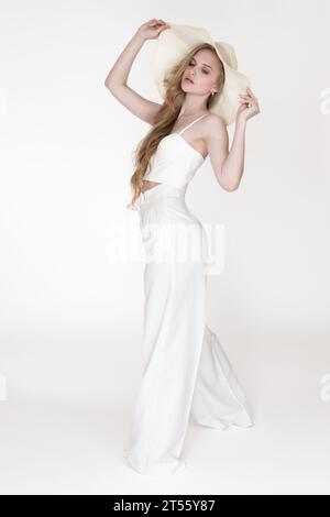 Modèle de mode féminin tenant le bord du chapeau de soleil souple avec les deux mains et regardant vers le bas. Pleine longueur shot femme blonde à la mode Banque D'Images