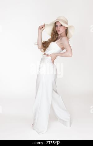 Jeune femme tenant le bord du chapeau de paille souple avec une main, met l'autre sur la hanche, posant et regardant la caméra. Femme à la mode habillée en haut corset Banque D'Images