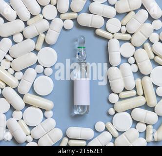 Mélange de capsules médicales blanches et pilules avec ampoule au milieu sur la vue de dessus bleu clair. Traitement médical. Produits pharmaceutiques assortis Banque D'Images