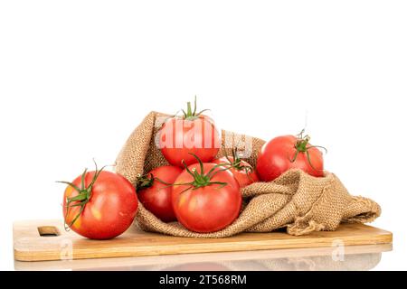 Plusieurs tomates juteuses roses dans un sac de jute sur une planche de cuisine en bois, macro, isolées sur fond blanc. Banque D'Images