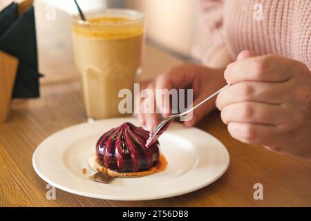 Femme mangeant délicieux gâteau de mousse de myrtille fraîche. Couper la texture du dessert en gros plan. Personne prenant une tranche de cheesecake pourpre dans un restaurant, c Banque D'Images