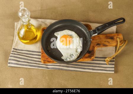 Oeuf frit avec de l'huile d'olive extra vierge dans une poêle avec une bouteille en verre avec de l'huile sur une planche de bois Banque D'Images