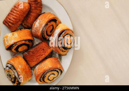 Brioches avec des graines de pavot sur une assiette sur un fond beige. Brioche maison sucrée. Vue de dessus. Banque D'Images