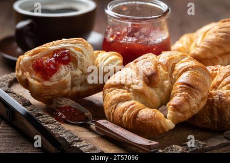Croissants avec conserves de fraises et tasse de café sur plateau en bois rustici Banque D'Images