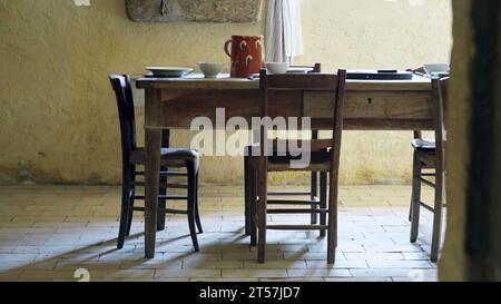 Rural intérieur de table rustique en bois et chaises exposées pour le déjeuner ou le dîner. Intérieur de ferme antique traditionnel avec assiettes et vase d'eau en s. Banque D'Images