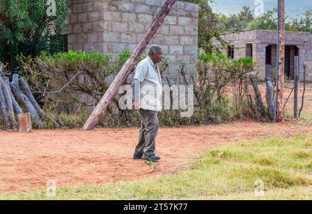 vieil homme africain marchant sur un chemin de terre dans le village, fumant une pipe Banque D'Images