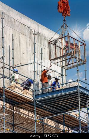 une équipe de travailleurs de la construction afro-américains sur l'échafaudage, attendant qu'une cage soit descendue par une grue Banque D'Images