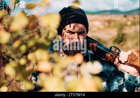 Chasseur barbu tenant une arme à feu et marchant dans la forêt. Chasseur avec fusil de chasse. Gros plan Portrait de Hamdsome Hunter. Banque D'Images