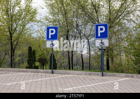 Deux panneaux de signalisation de stationnement handicapés fixés sur des poteaux. Marquages routiers pour les places de stationnement sur les pavés. Banque D'Images