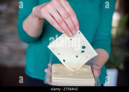 La main d'une femme prend un morceau de fromage d'un paquet en gros plan. Préparation pour la journée des amateurs de fromage. Banque D'Images