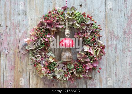 couronne d'hortensia fklows, hanches roses et baies de lierre accrochées au mur en bois Banque D'Images