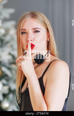 Photo de jeune femme blonde cheveux bouclés lèvres secret signe doigt Banque D'Images