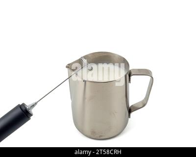 Appareil automatique de fabrication de mousse de lait. Tasse à lait en métal et mousseur à lait électrique isolé sur fond blanc. Banque D'Images