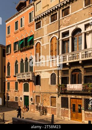 Maisons de Venise en Italie. Deux personnes sont assises dans un portique tandis qu'une troisième personne erre dans la rue. La couleur ocre prédomine. Banque D'Images