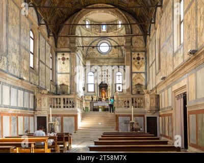 Intérieur d'une église vénitienne richement décorée de marbre. Deux touristes sont assis dans l'église tandis qu'un touriste contemple l'autel. Venise. Banque D'Images