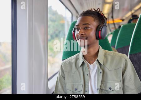Jeune homme se rendant au travail assis dans un train portant un casque sans fil Banque D'Images