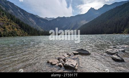 Une vue panoramique sur un plan d'eau tranquille entouré de majestueux sommets montagneux, avec des rochers déchiquetés dépassant du bord de l'eau Banque D'Images