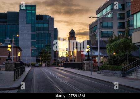 Architecture de bâtiments magnifiques, moder et vintage. Lampadaires illuminés au coucher du soleil sur George Dock Street avec des lignes de tramway, Dublin, Irlande Banque D'Images