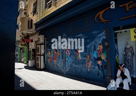 Fresque Street art vibrante ornant la façade arrière d'un magasin de vêtements tendance, avec des femmes de dessins animés chics frappant des poses au milieu de ruines fantaisistes. Banque D'Images