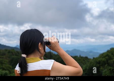 Jeune femme avec des jumelles sur la montagne par une journée ensoleillée. Femme utilisant des jumelles lors de la randonnée. Femme de randonnée utilise des jumelles pour voyager et a un Banque D'Images