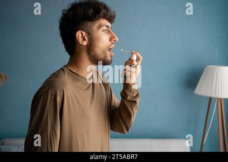 Homme arabe malade à la bouche ouverte utilisant un spray pour gorge contre une toux sèche. Traités à domicile. Maladies saisonnières Banque D'Images