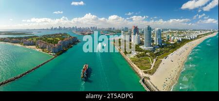 Navire porte-conteneurs commercial entrant dans le port de Miami par le canal principal près de South Beach. Hôtels luxueux et bâtiments résidentiels sur le front de mer Banque D'Images