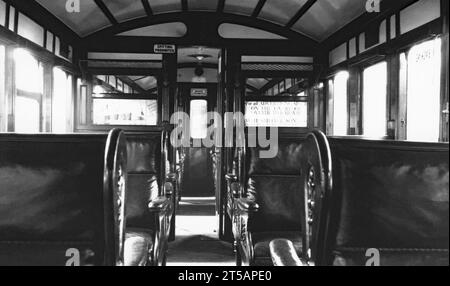 L'intérieur d'un wagon de première classe sur les trains électriques à carrosserie en bois sur le Liverpool Overhead Railway, Merseyside, Angleterre, Royaume-Uni vers 1950. Les sièges sont revêtus de cuir et les panneaux dans la voiture indiquent «ne pas fumer» et «ne pas cracher». Le Liverpool Overhead Railway opérait le long des quais de Liverpool et ouvrit ses portes en 1893. C’était le premier chemin de fer électrique surélevé au monde et le deuxième plus ancien métro électrique au monde. À son apogée, près de 20 millions de personnes utilisaient le chemin de fer chaque année. Un rapport de 1955 a montré qu'il nécessitait des réparations inabordables et le chemin de fer a fermé en 1956. Banque D'Images